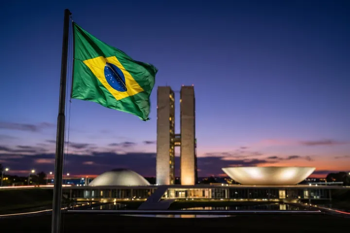 Congresso Nacional em Brasília ao anoitecer, com a bandeira do Brasil em primeiro plano