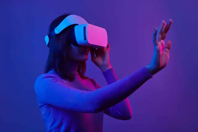 Jovem com um óculos branco de realidade virtual e uma mão estendida, sob uma luz violeta e rosada que sugere um ambiente digital
