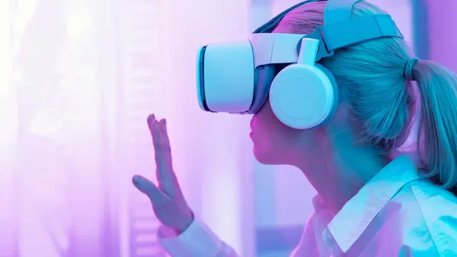 Mulher com óculos de realidade virtual e fones de ouvido levantando uma mão, em um ambiente iluminado de rosa e violeta