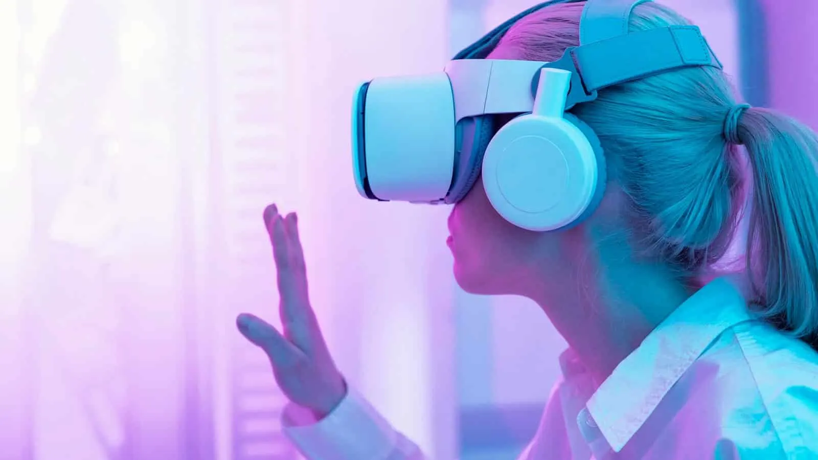 Mulher com óculos de realidade virtual e fones de ouvido levantando uma mão, em um ambiente iluminado de rosa e violeta