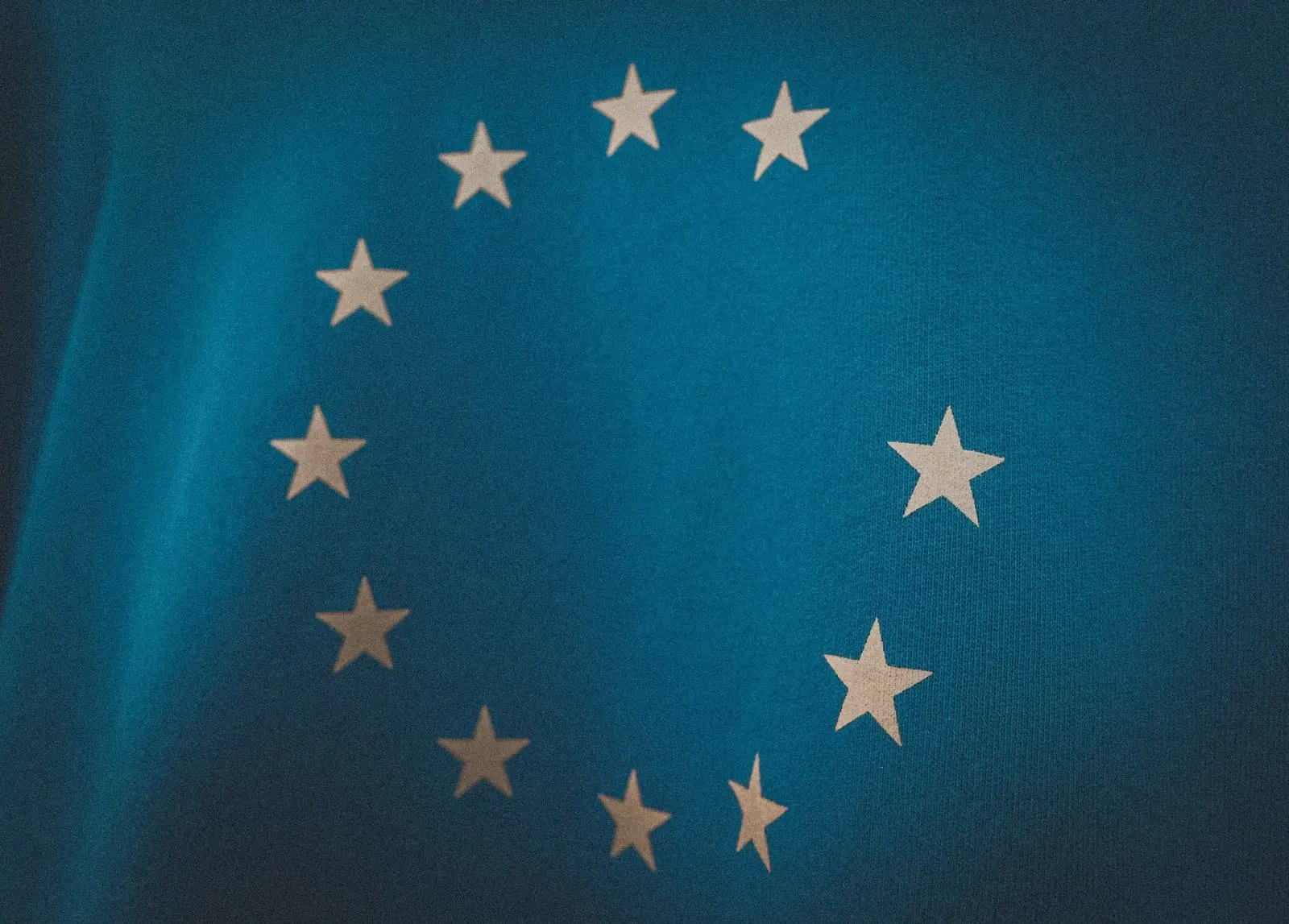 Bandeira da União Europeia, com seu círculo de estrelas brancas sobre fundo azul, em uma foto próxima e escura