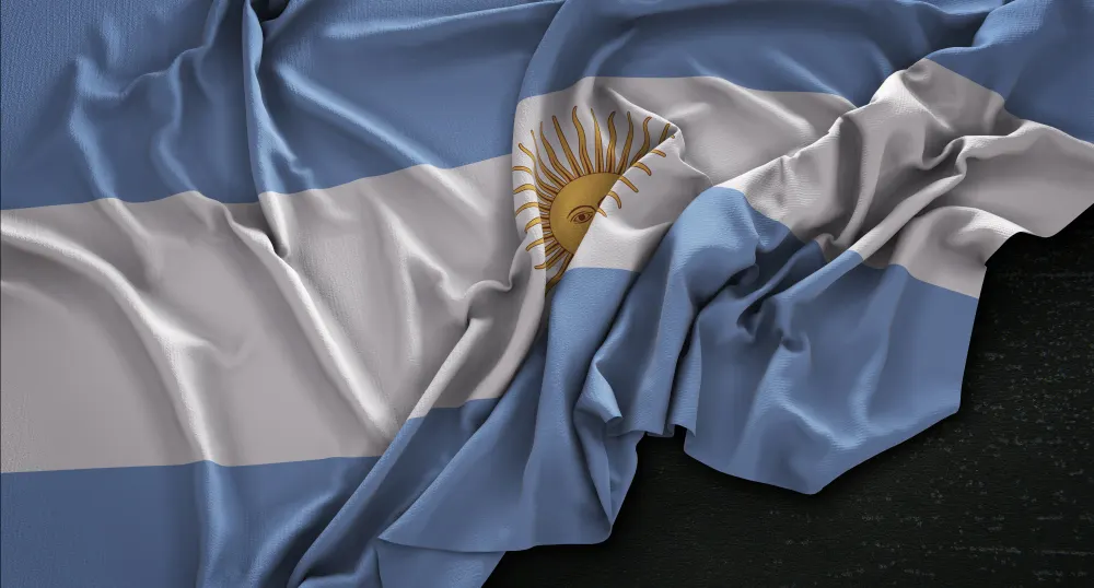 Bandeira argentina azul-clara e branca com o sol dourado, amassada e apoiada sobre um fundo escuro.
