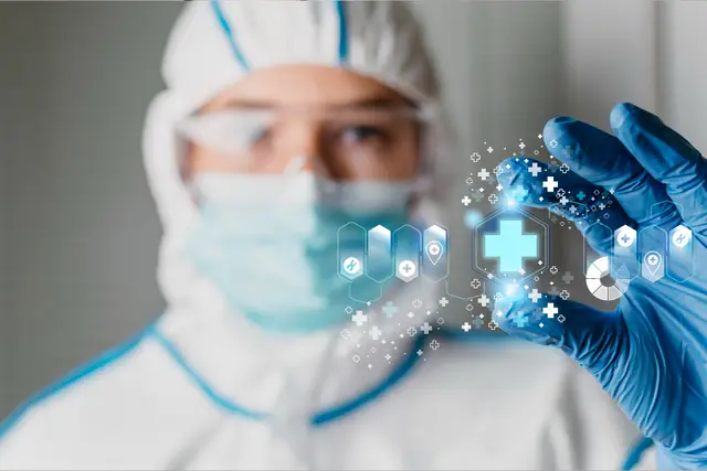 Profissional com traje de proteção, máscara e luvas azuis segura diante da câmera um símbolo médico luminoso rodeado de ícones.