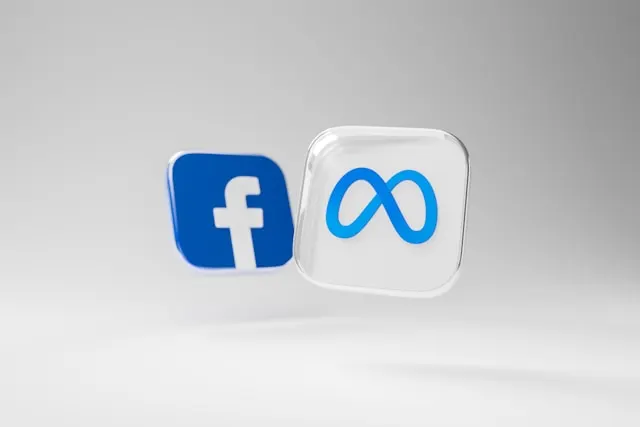 Dois ícones 3D flutuando sobre fundo cinza claro: o logotipo azul do Facebook e o símbolo de infinito da Meta em um cubo translúcido.