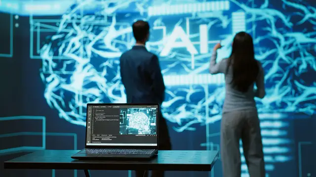 Um homem de terno e uma mulher de costas diante de um grande cérebro luminoso com as letras AI, com um notebook em primeiro plano.