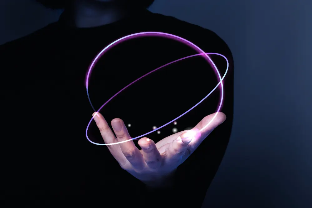 Uma mão aberta de uma pessoa vestida de preto segura um anel duplo luminoso violeta que forma uma esfera.