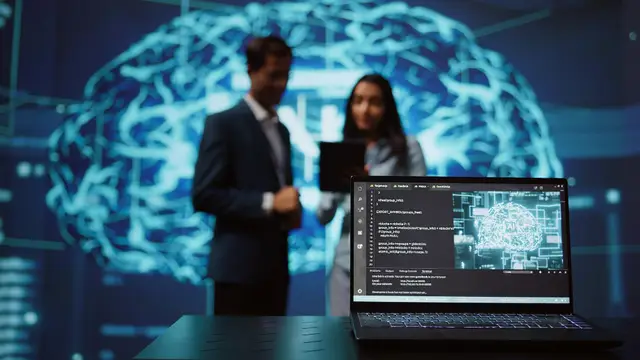 Um homem e uma mulher de pé, desfocados, diante da projeção luminosa de um cérebro, com um notebook com código em primeiro plano
