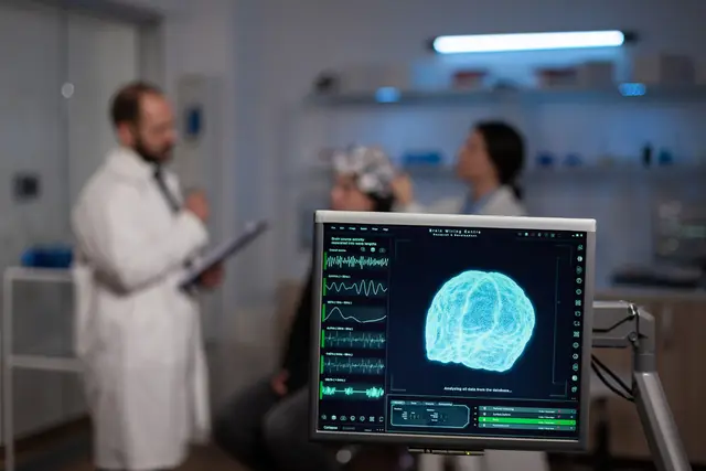 Cientista de jaleco e uma paciente com touca de eletrodos ao fundo, com um monitor em primeiro plano que mostra um cérebro em 3D