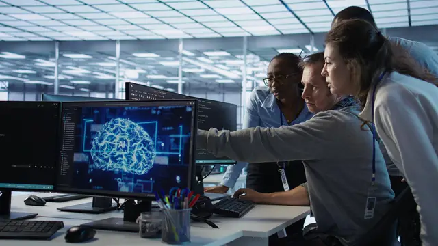 Uma equipe de profissionais observa um monitor que mostra um cérebro digital com as letras AI em um escritório iluminado