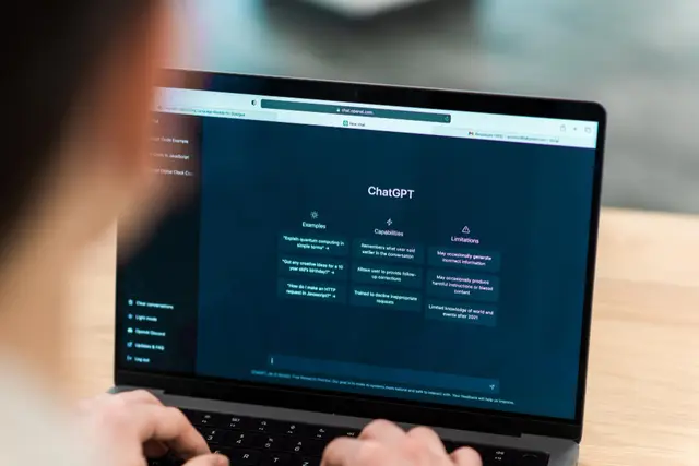 Pessoa digitando em um laptop com a tela inicial do ChatGPT, que mostra exemplos, capacidades e limitações do chatbot