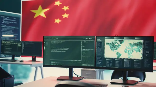 Bandeira da China atrás de dois monitores com código e um mapa, sobre uma mesa de trabalho