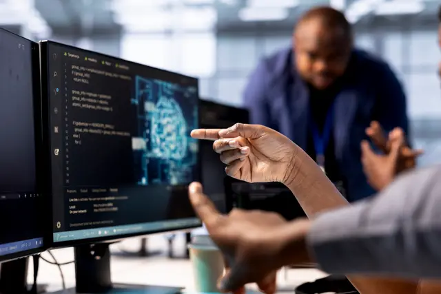 Várias pessoas apontam para um monitor com um cérebro digital e código enquanto conversam em uma sala de trabalho
