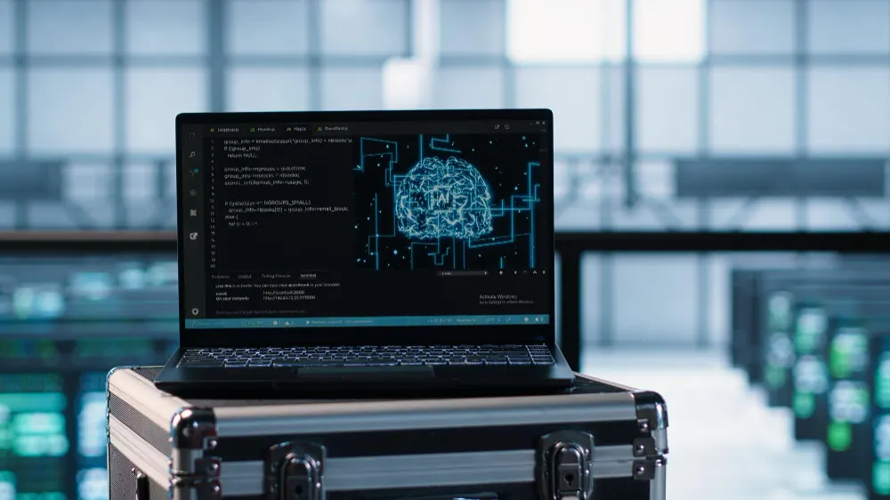 Notebook sobre uma maleta metálica com um cérebro digital na tela, diante de servidores