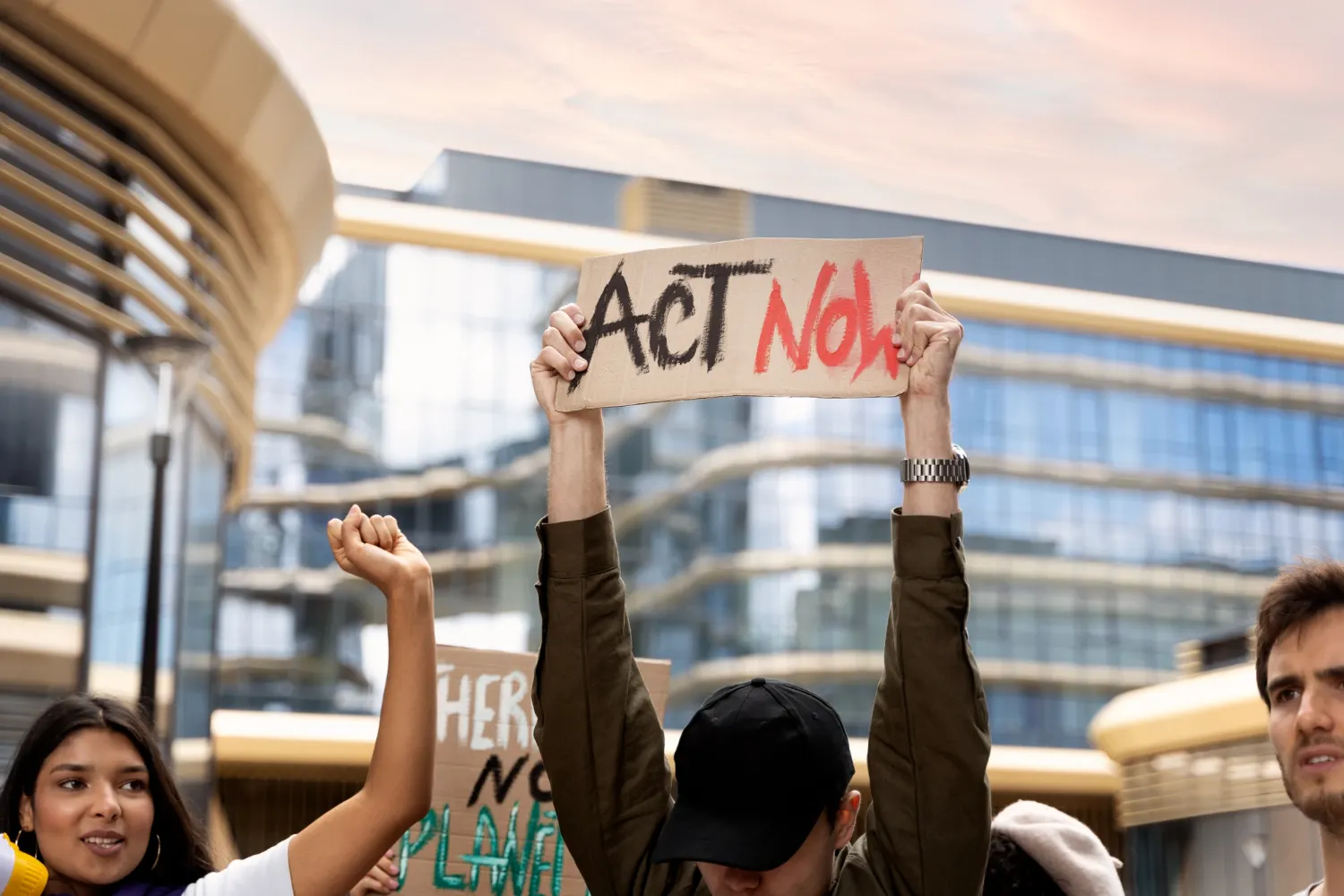 Manifestantes com um cartaz que diz «Act Now» diante de edifícios de escritórios modernos