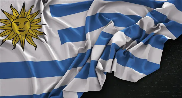 Bandeira do Uruguai com o Sol de Maio, ondulada e em primeiro plano sobre uma superfície escura