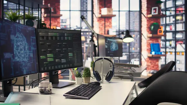 Mesa de trabalho com vários monitores que mostram um cérebro digital e código, em um escritório iluminado