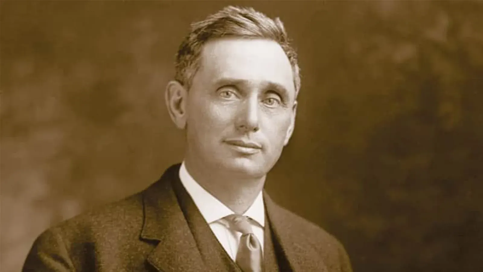 Retrato em sépia de um homem de cabelo curto com terno escuro, camisa branca e gravata, imagem do juiz Louis Brandeis