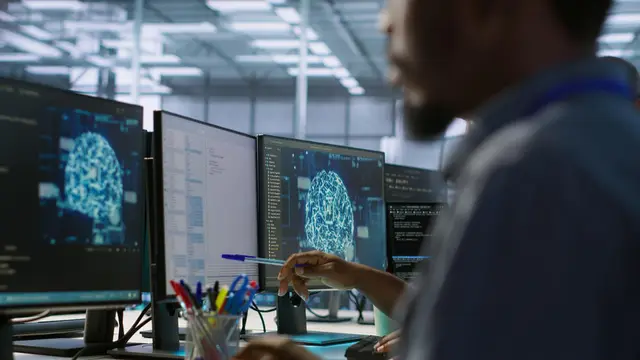 Um homem trabalha diante de vários monitores que exibem imagens geradas de um cérebro, em um escritório de tecnologia
