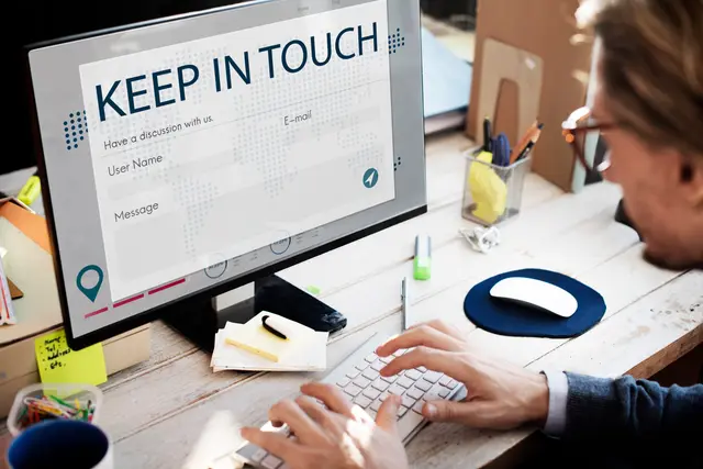 Homem de óculos digitando em um teclado diante de um monitor com um formulário de contato intitulado «Keep in touch»