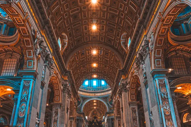Interior de uma basílica com abóbada de caixotões, arcos e colunas ornamentadas sob luzes quentes